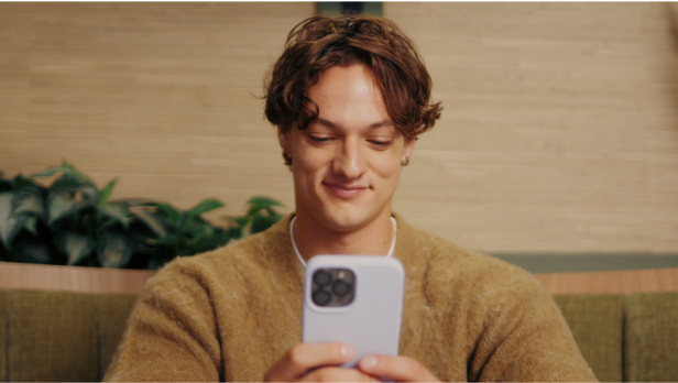 A young person in an orange sweater smiles at something they've just received on their phone.