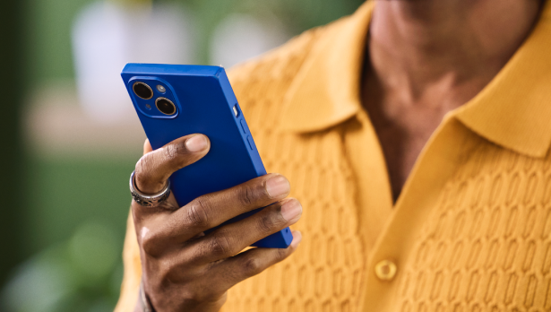 A person in a mustard-colored sweater holds a bright blue mobile phone.