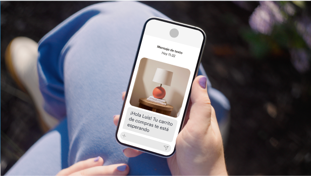 Una persona con esmalte de uñas lavanda sostiene un teléfono móvil. Recibieron un código promocional personalizado con un 20% de descuento de un minorista junto con una foto de producto de una lámpara de mesa roja.